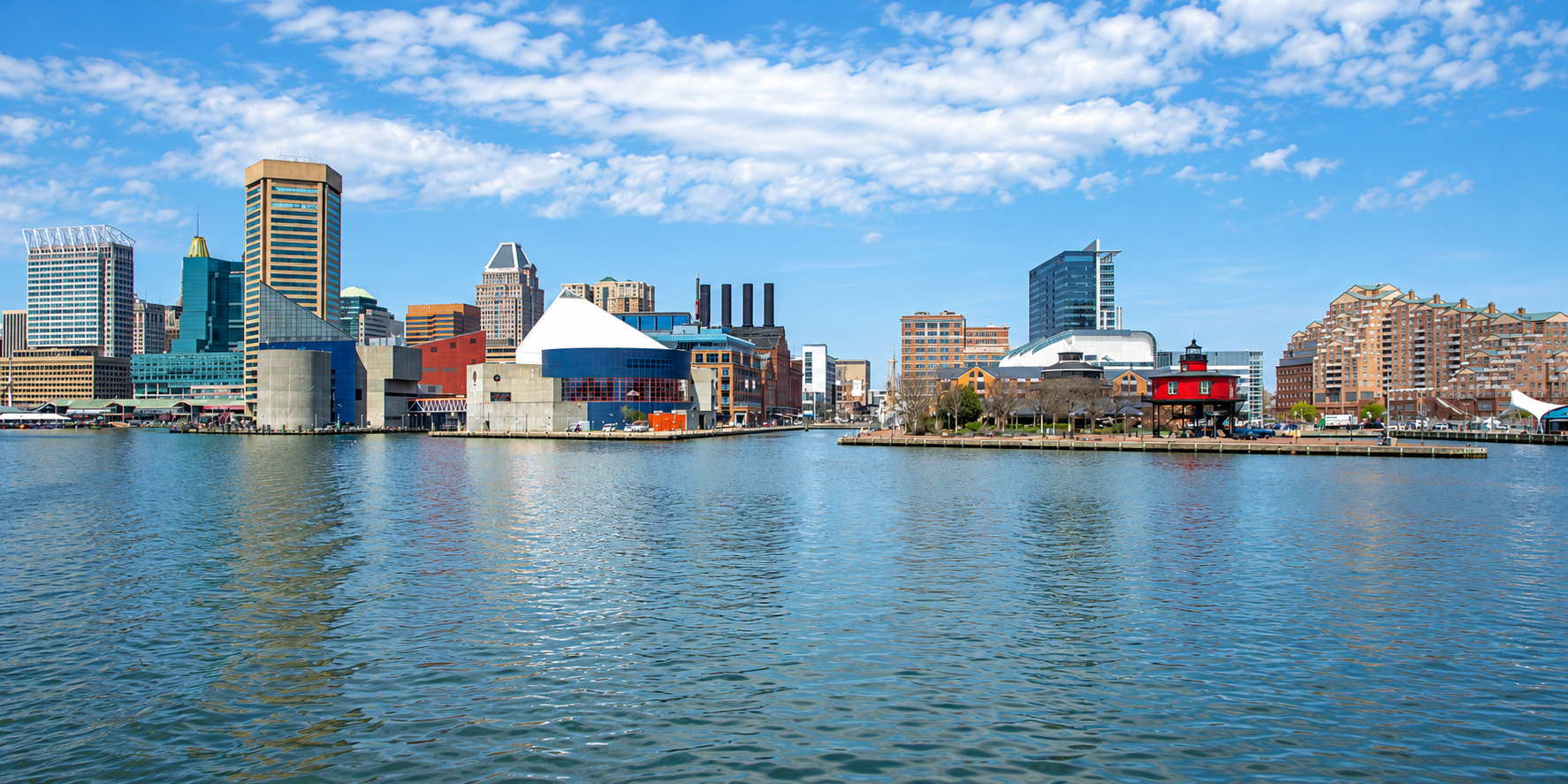 Baltimore Inner Harbor skyline with waterfront buildings and the red Seven Foot Knoll Lighthouse.