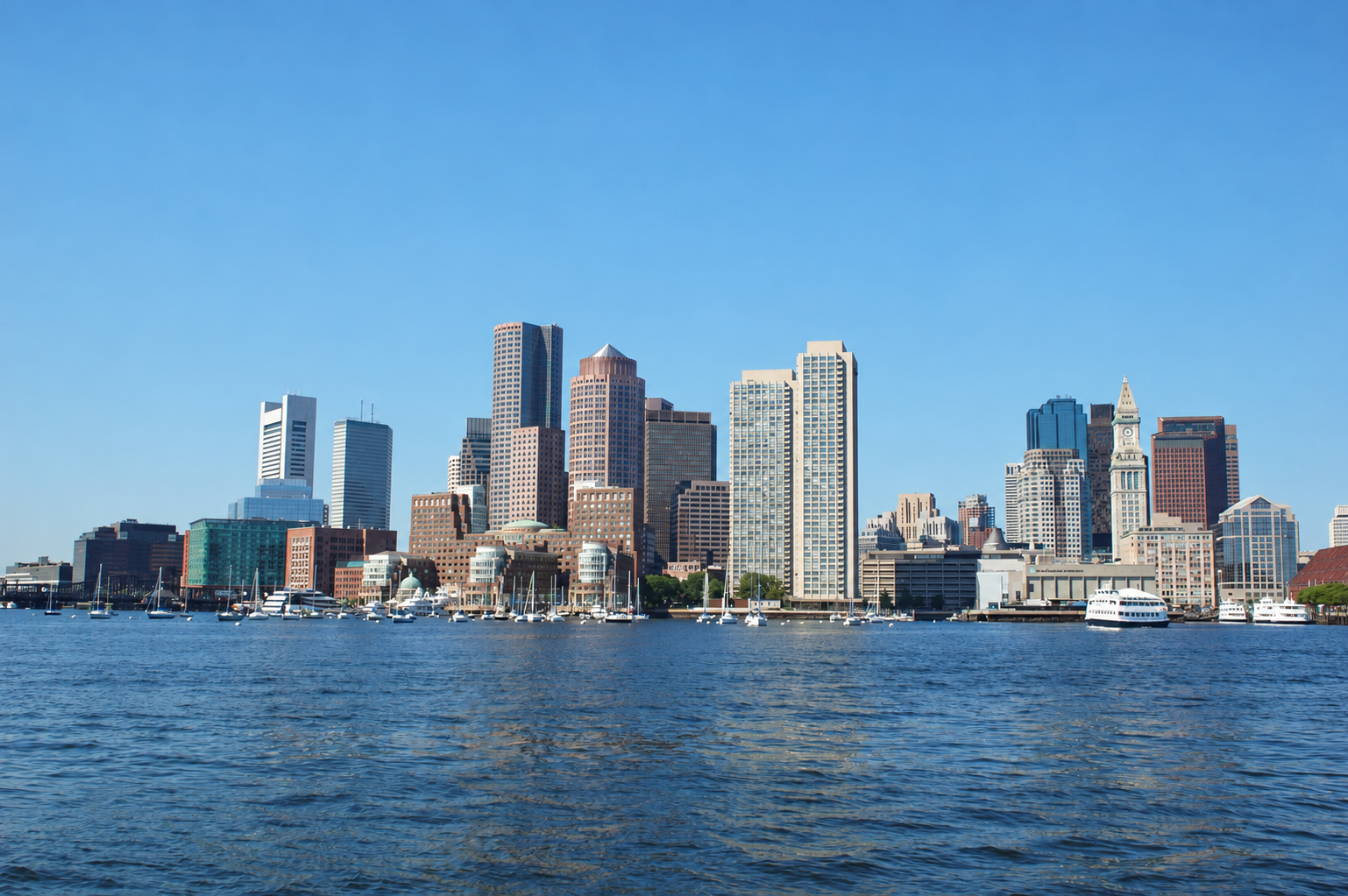 Boston waterfront skyline and moored sailboats viewed across the harbor.
