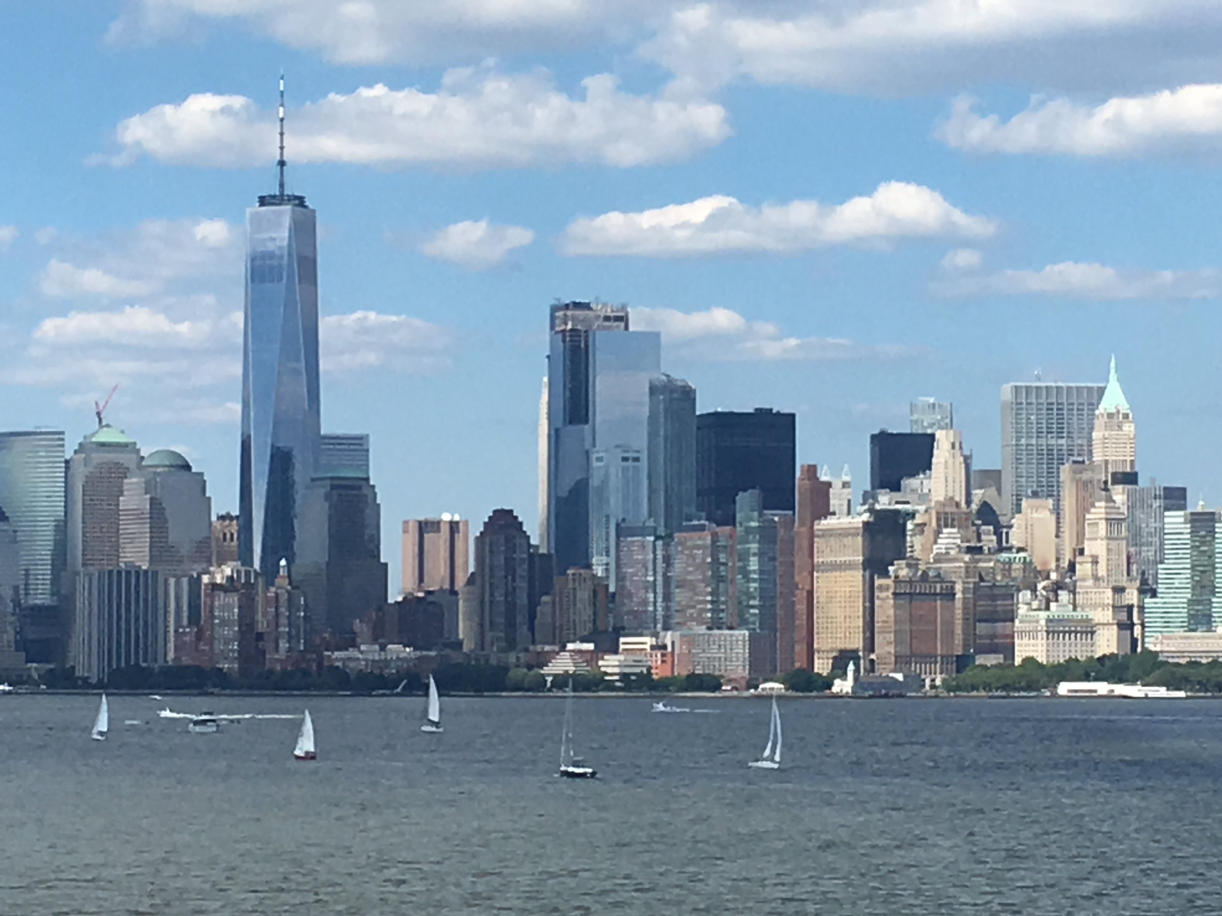 Lower Manhattan skyline and sailboats seen across New York Harbor from Liberty Island.