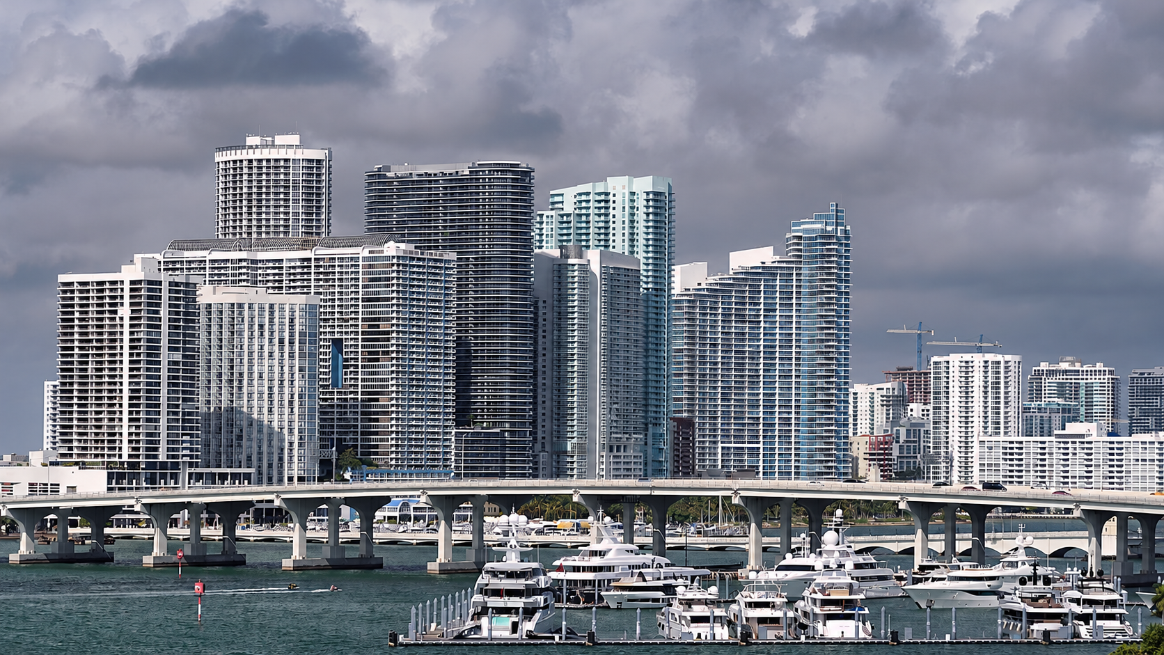 Miami waterfront towers, bridge and marina under cloudy skies.