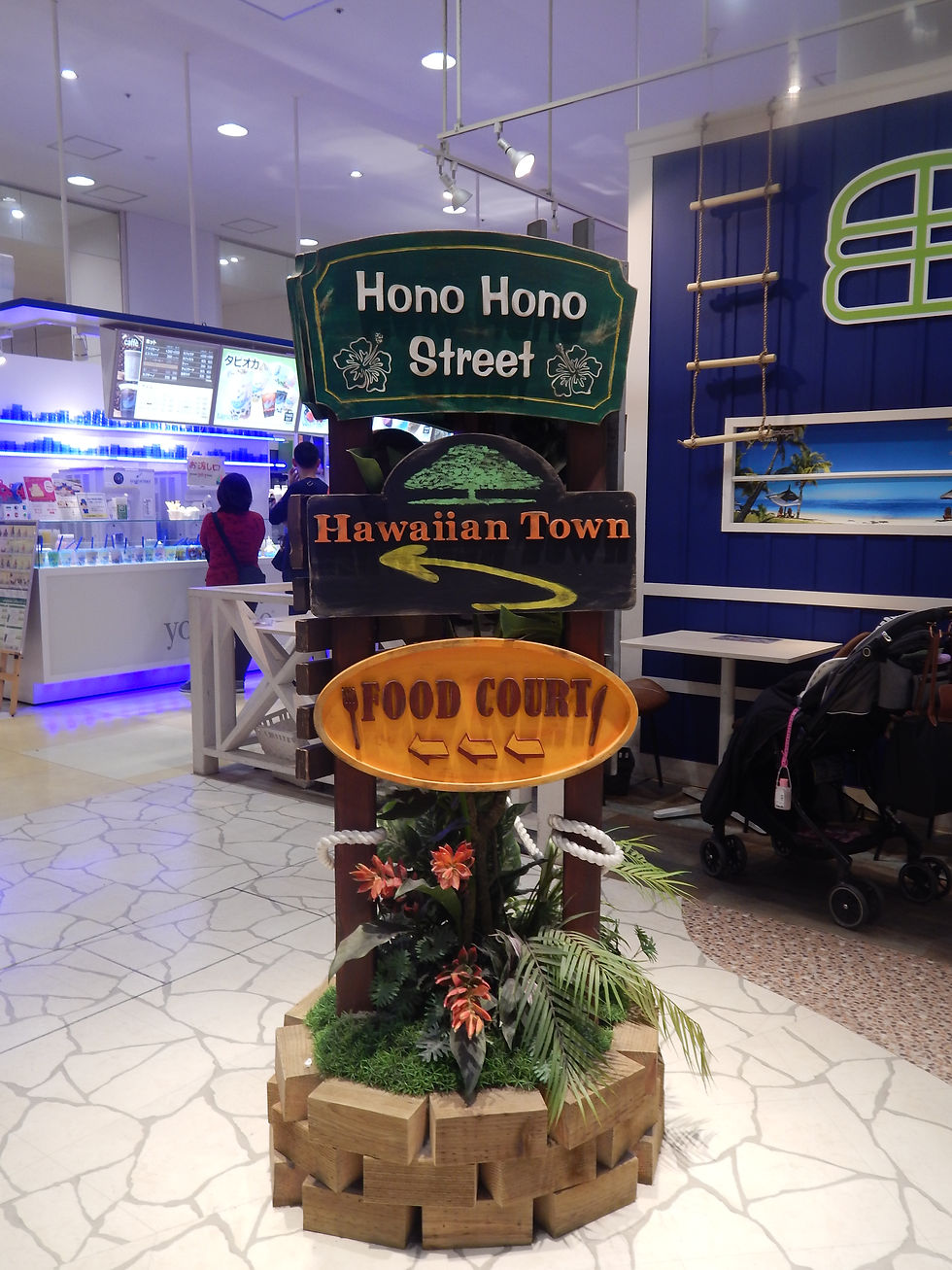 a display with various signs that say, "Hono Hono Street", "Hawaiian Town" and Four court" all surrounded by fake tropical flora