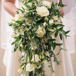 A stunning winter wedding bouquet featuring white roses, pinecones, and seasonal greenery.