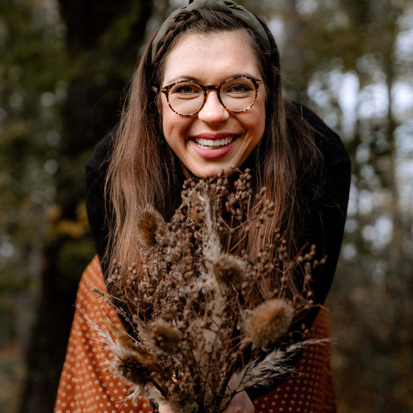 Autumn-themed maternity shoot in the Bad Pyrmont Forest. Woman adorned with dried flowers leans forward, smiling at the camera.