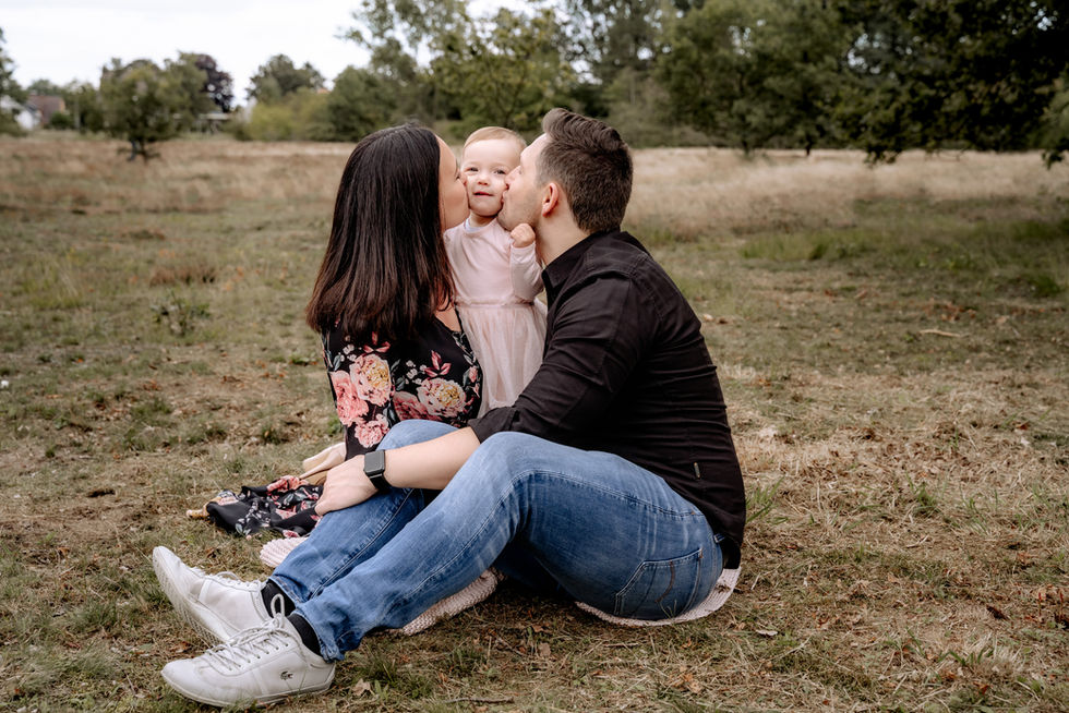 Mama und Papa küssen ihre kleine Tochter von beiden Seiten auf die Wange. Familien-Shooting auf einem Feld in der Nähe von Syke.