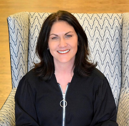 Smiling woman in black zip-up jacket sits in a chair Collage Salon.