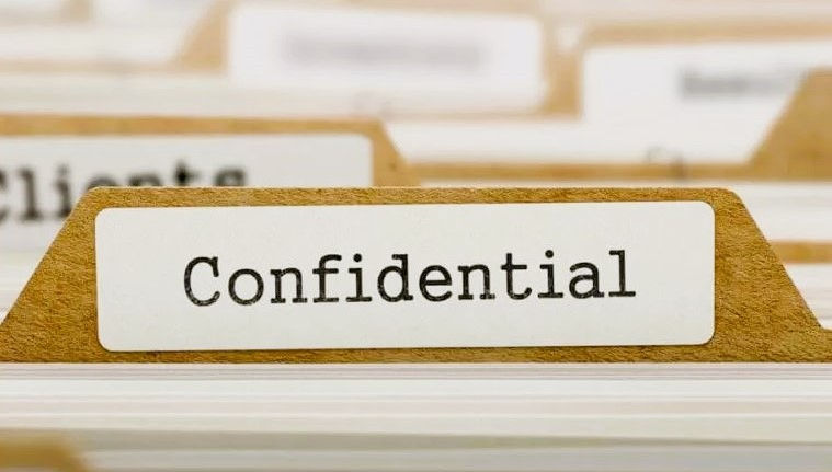 alt="Silhouettes of three men in a conference room standing around a desk and discussing confidentiality"