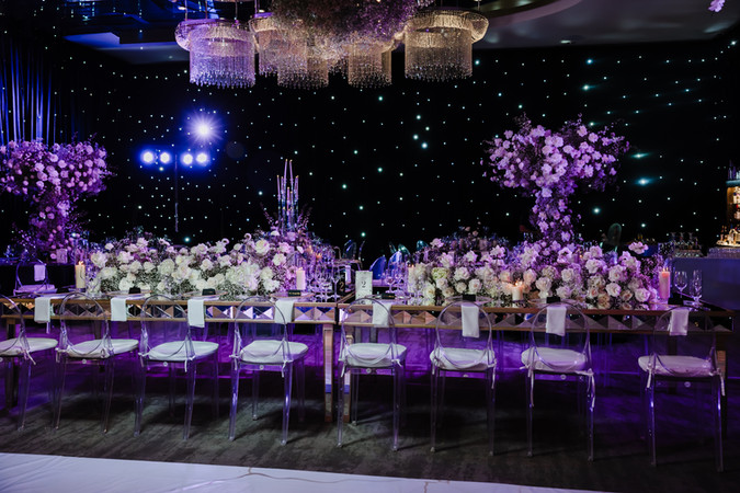 Lavish Garza Blanca Cancun wedding reception setup featuring long mirrored tables adorned with white roses, baby’s breath, and candles, under cascading crystal chandeliers and a starlit black backdrop for a glamorous ambiance.