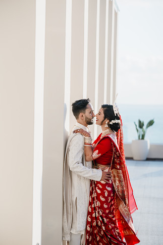 Indian bride in a red and gold saree and groom in an ivory sherwani share a joyful, intimate moment against a modern architectural backdrop at Garza Blanca Cancun during their destination wedding