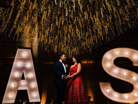 Elegant Indian couple during wedding reception at Hard Rock Punta Cana, standing under floral ceiling décor and marquee initials A and S.