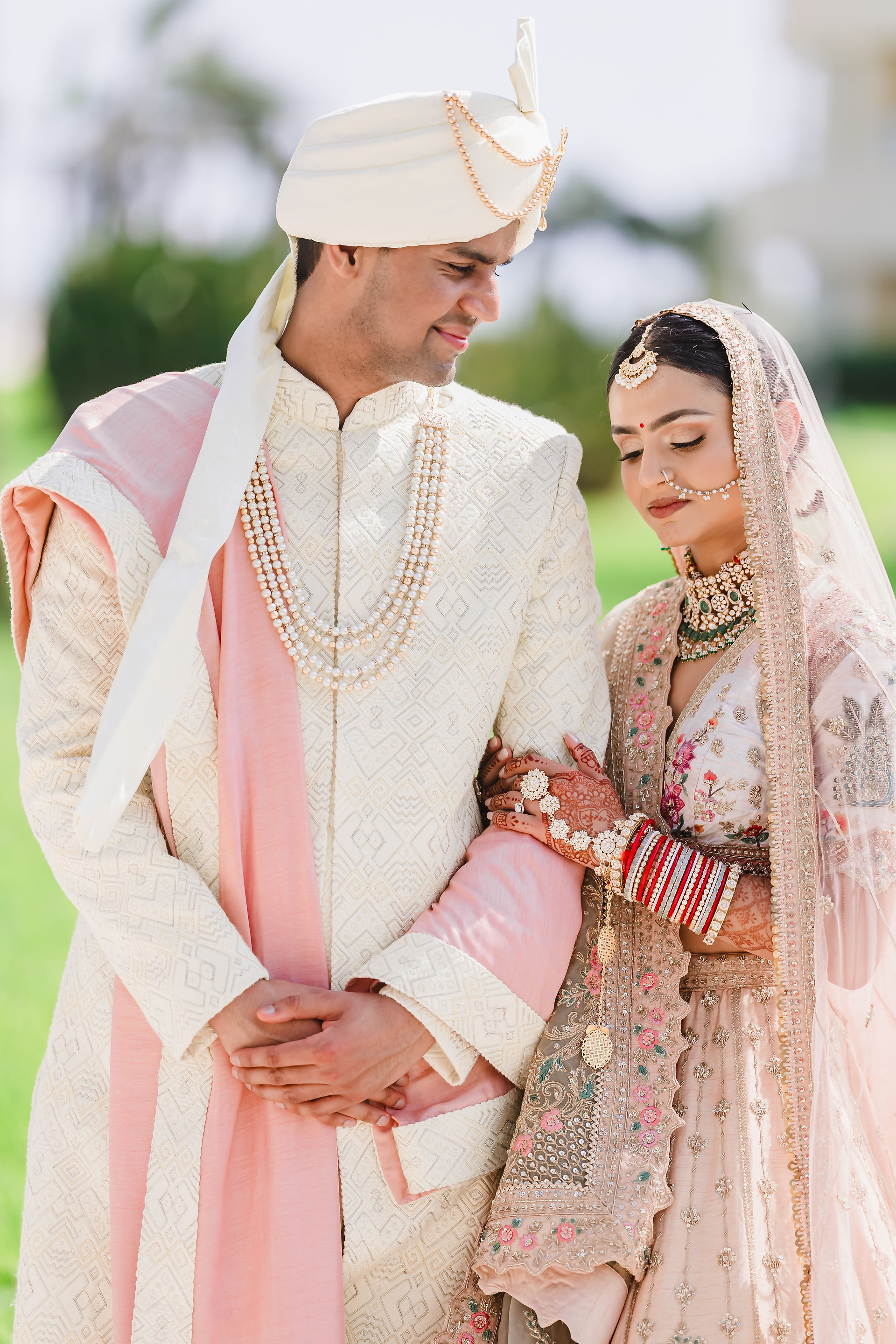  Groom Rishabh in ivory sherwani with pearl malas smiles tenderly at bride Devina, who leans on his arm in a pastel embroidered lehenga and red bridal bangles during their first look at Moon Palace Cancún.
