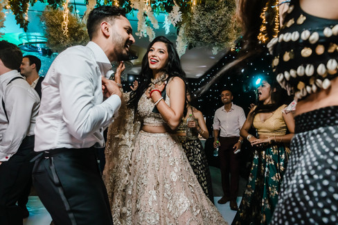 Bride and groom laughing and dancing together during their Garza Blanca Cancun wedding reception, surrounded by friends under floral ceiling décor and twinkling lights.