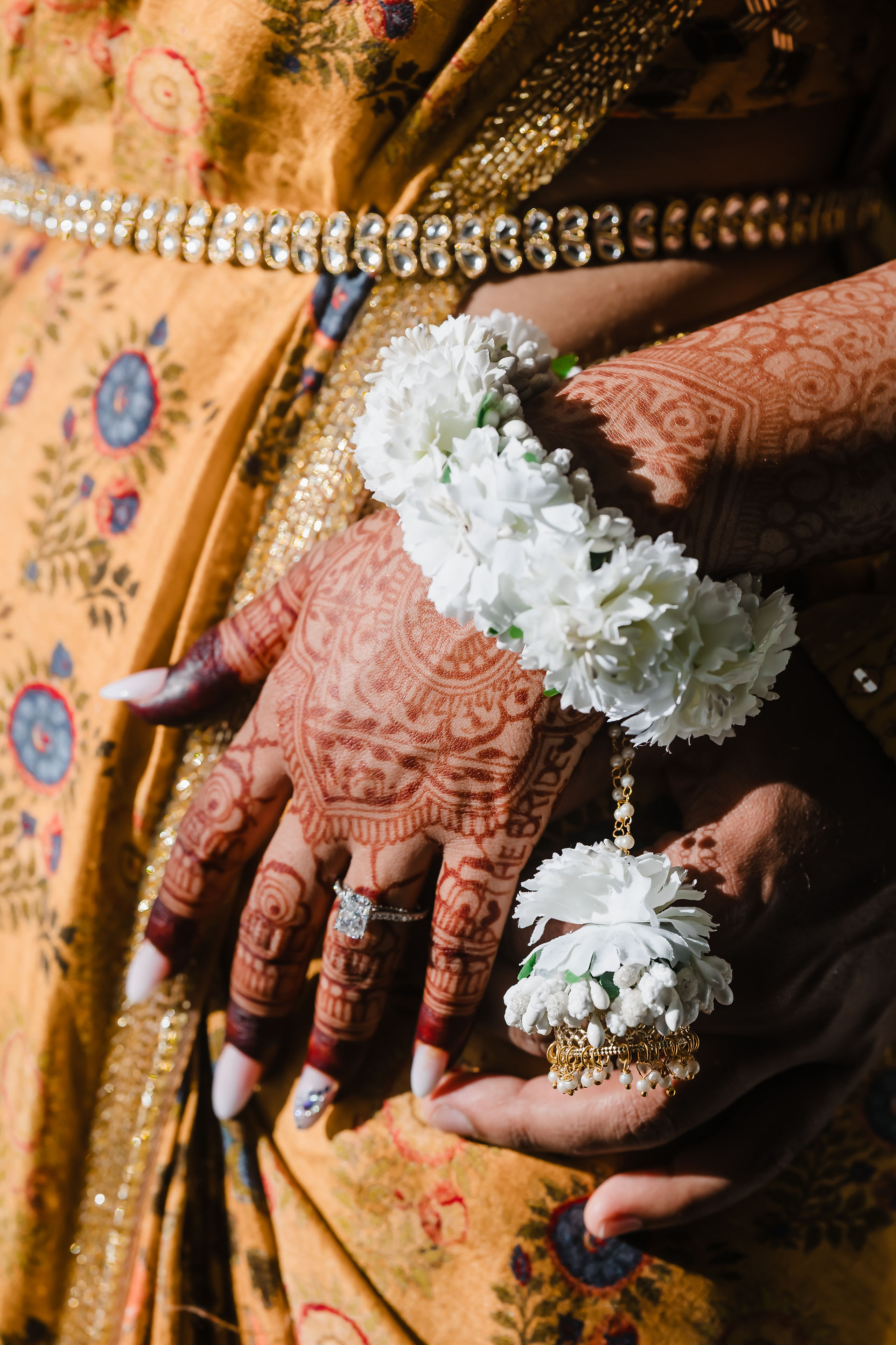 Close-up of Rhia’s mehndi-adorned hands with white floral jewelry and diamond engagement ring during her Pithi and Haldi at Garza Blanca Cancun, wearing a golden patterned saree.
