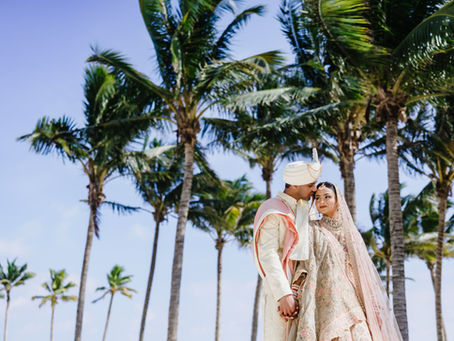 ndian bride and groom in elegant traditional wedding attire sharing a tender moment beneath tropical palm trees at Moon Palace Cancún during their destination wedding in Mexico