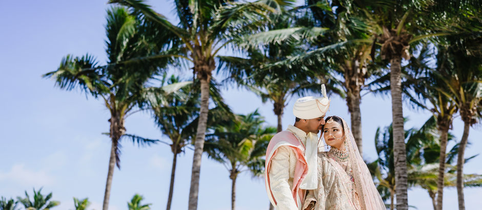 ndian bride and groom in elegant traditional wedding attire sharing a tender moment beneath tropical palm trees at Moon Palace Cancún during their destination wedding in Mexico