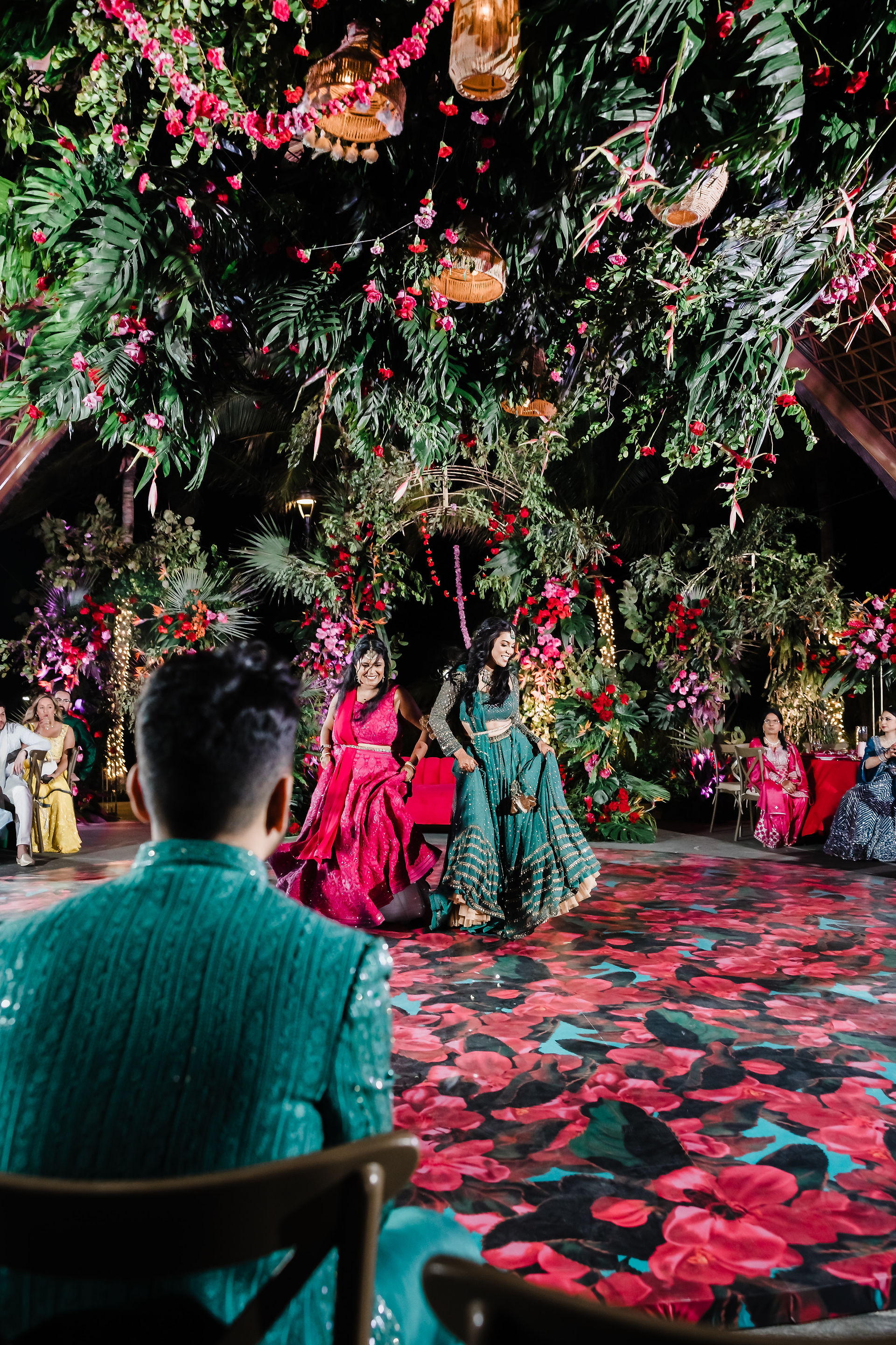 Indian bride in green lehenga walking towards groom under lush floral canopy during Sangeet at Garza Blanca Cancun.