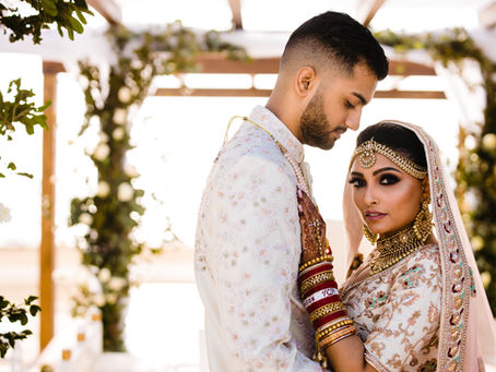 Romantic portrait of an Indian bride and groom in traditional wedding attire under a floral canopy at a luxury resort in Cancun, perfect for a destination Indian wedding.