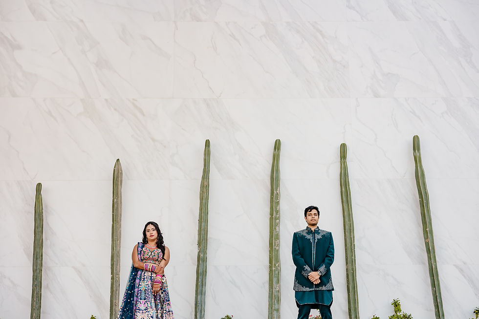 Indian wedding couple standing apart against a marble wall lined with tall cacti in Los Cabos.