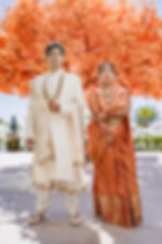 ndian couple in traditional wedding outfits standing under vibrant orange tree at Garza Blanca Los Cabos.