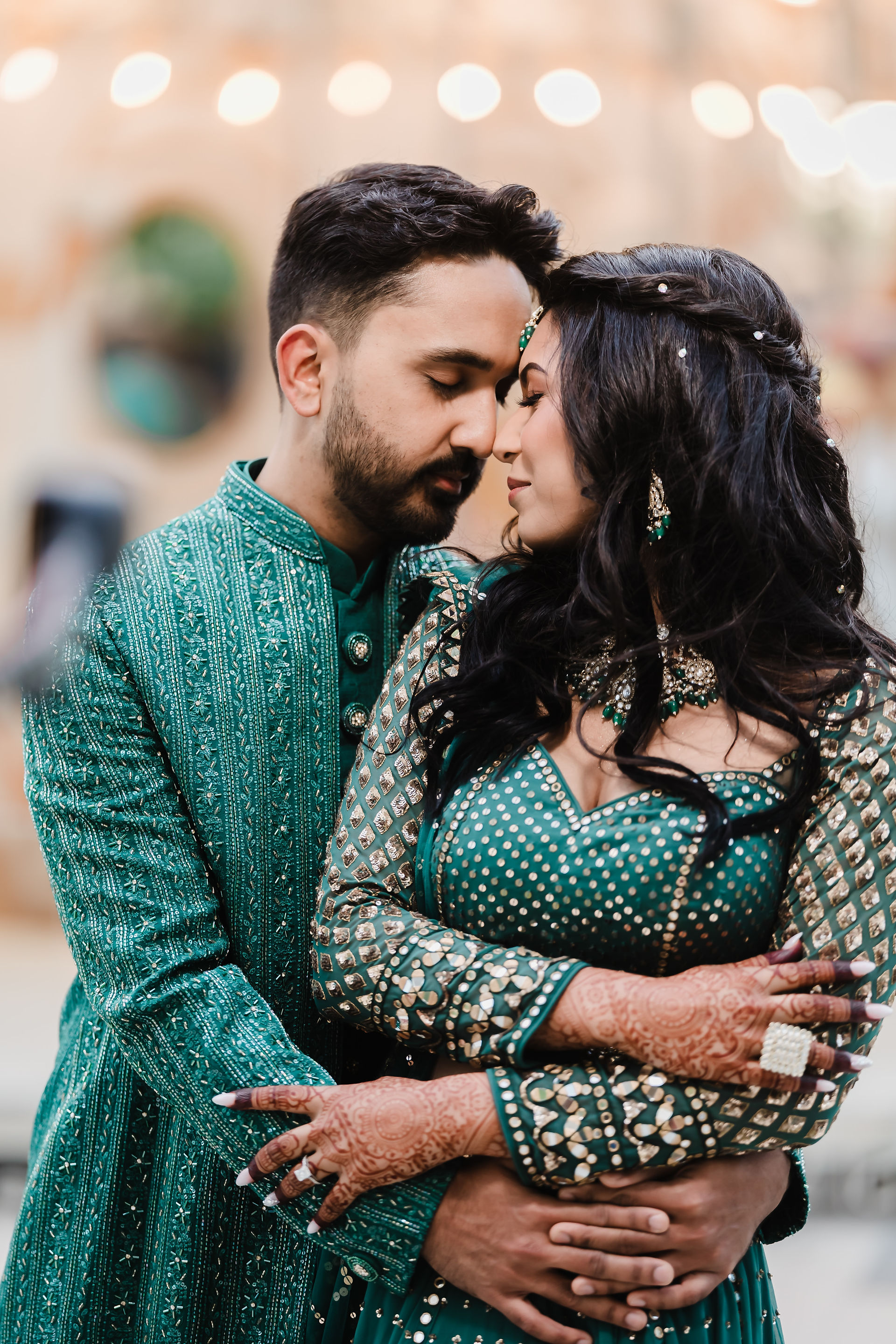 Groom in an emerald green sherwani embracing his bride in a matching green outfit during their Indian destination wedding at Garza Blanca Cancun.