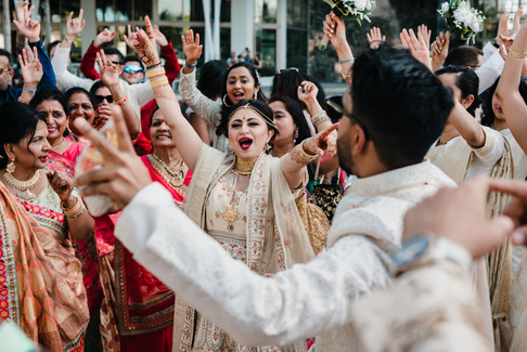 Bride joyfully dancing with family and friends during the baraat at Garza Blanca Cancun, wearing an ivory and gold lehenga with traditional jewelry, surrounded by vibrant red and gold sarees.