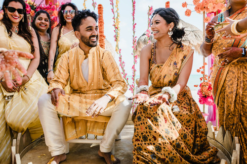 Bride and groom sharing a joyful moment during their Haldi ceremony at Garza Blanca Cancun, surrounded by friends in colorful sarees with the beach and floral décor in the background.