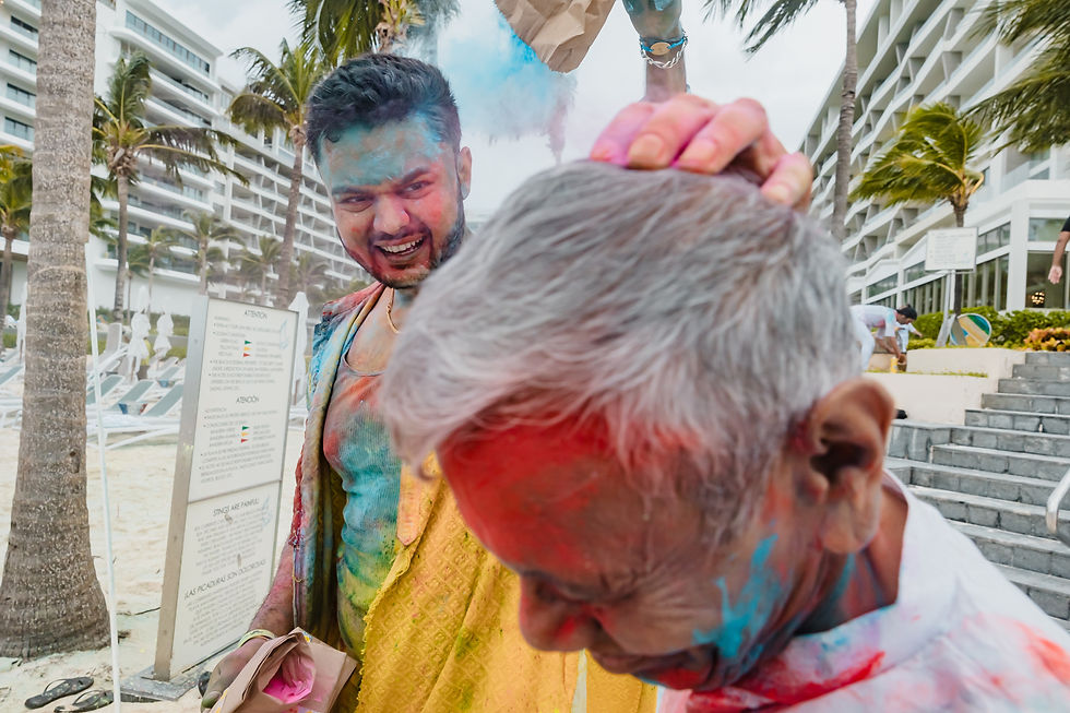 Family members celebrating with vibrant colors during a Holi-inspired event at an Indian destination wedding in Mexico. Covered in bright powders of blue, pink, yellow, and green, guests laugh and enjoy the festive atmosphere at a beachfront resort. This candid photo captures the joy, culture, and lively traditions that make South Asian weddings in Cancun, Los Cabos, Puerto Vallarta, and the Riviera Maya so unique.