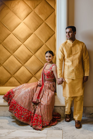 Devina in a peach lehenga with red embroidery seated against a golden quilted wall, holding hands with Rishabh in a yellow kurta at their Haldi ceremony in Moon Palace Cancún.