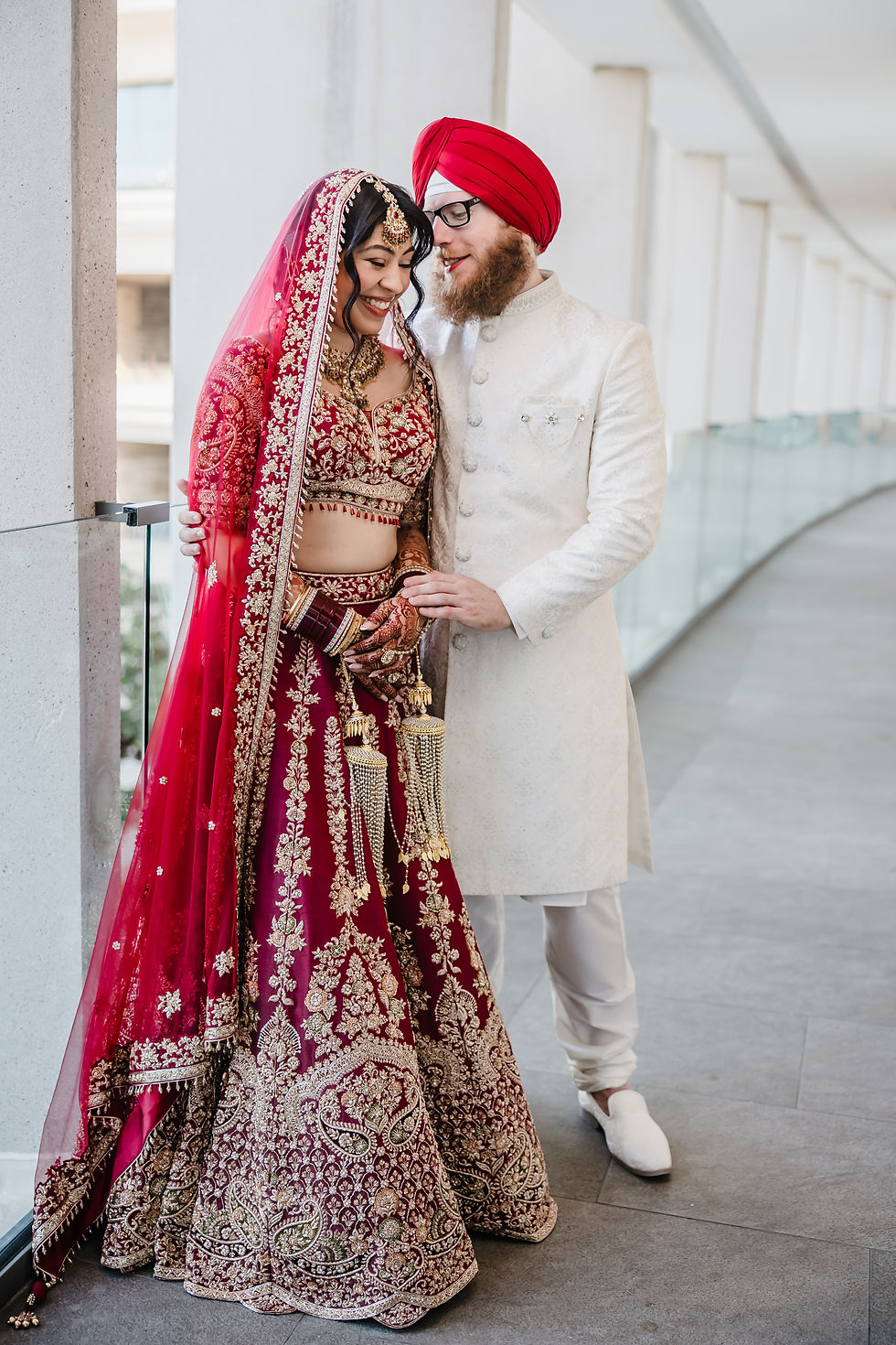 Sikh groom in ivory sherwani and red turban with Hindu bride in red lehenga smiling at Dreams Bahia Mita