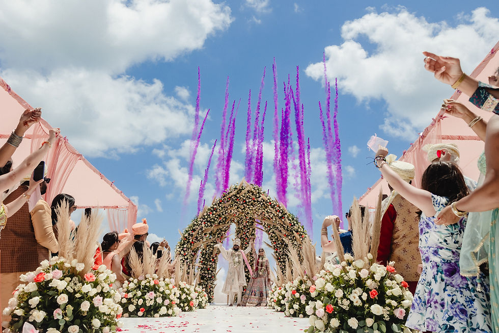 Bride and groom recessing under a floral mandap with pink smoke cannons and cheering guests during a vibrant Indian wedding ceremony at Venado beach in Moon Palace Cancún