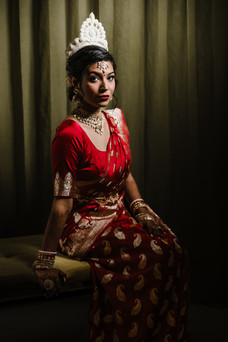 Elegant Indian bride in a traditional red and gold Bengali saree, adorned with intricate jewelry and a white mukut headpiece, poses gracefully before her wedding at Garza Blanca Cancun.
