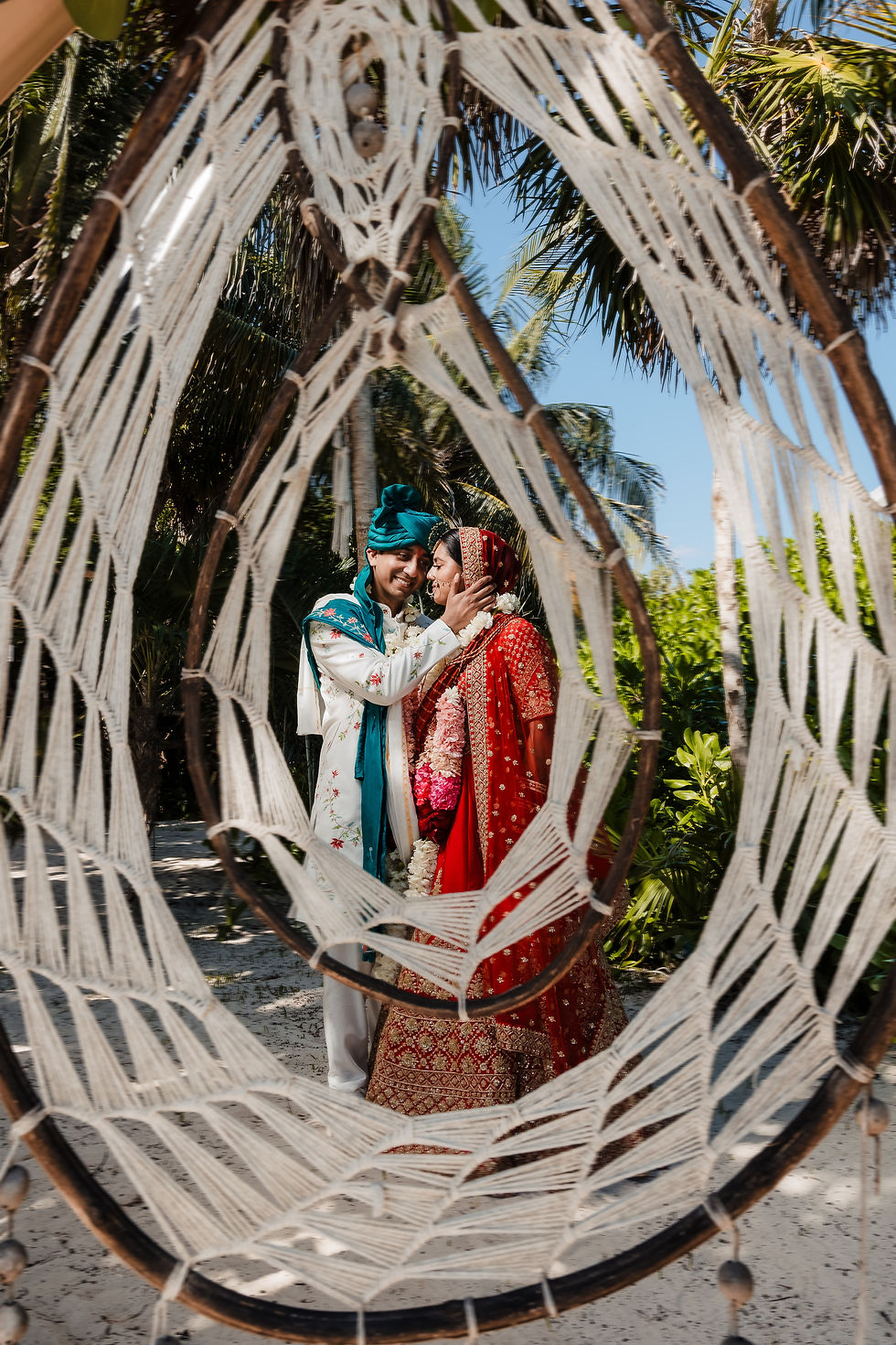 Indian bride and groom portrait framed through macrame swing at Paradisus Playa del Carmen beach wedding