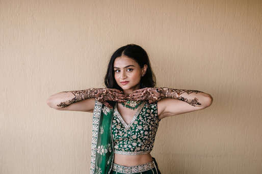 Bride in emerald green lehenga shows intricate mehndi designs before Indian wedding.