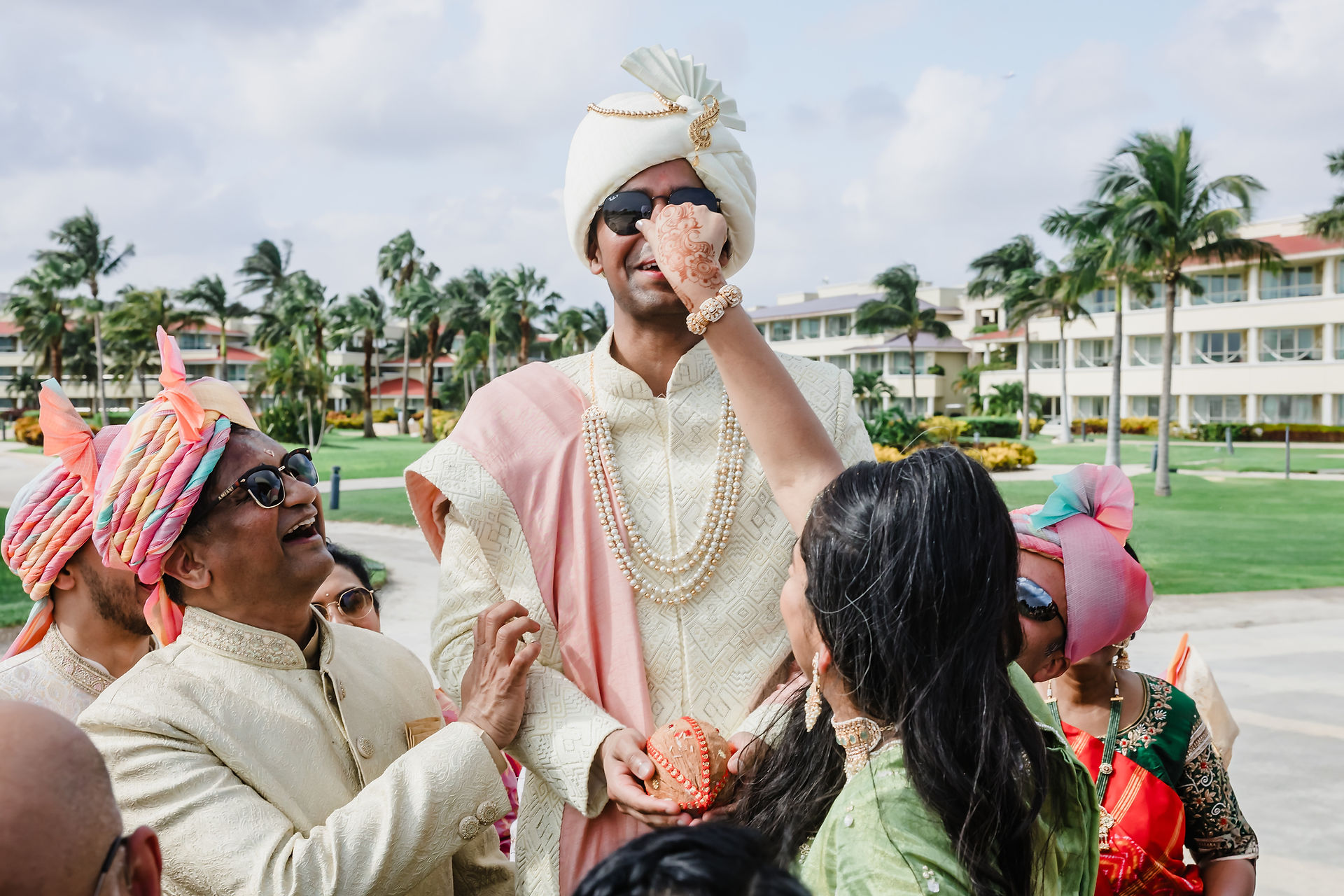 Groom Rishabh in ivory sherwani and blush stole receives tilak during wedding rituals at Moon Palace Cancún, surrounded by family in colorful turbans.