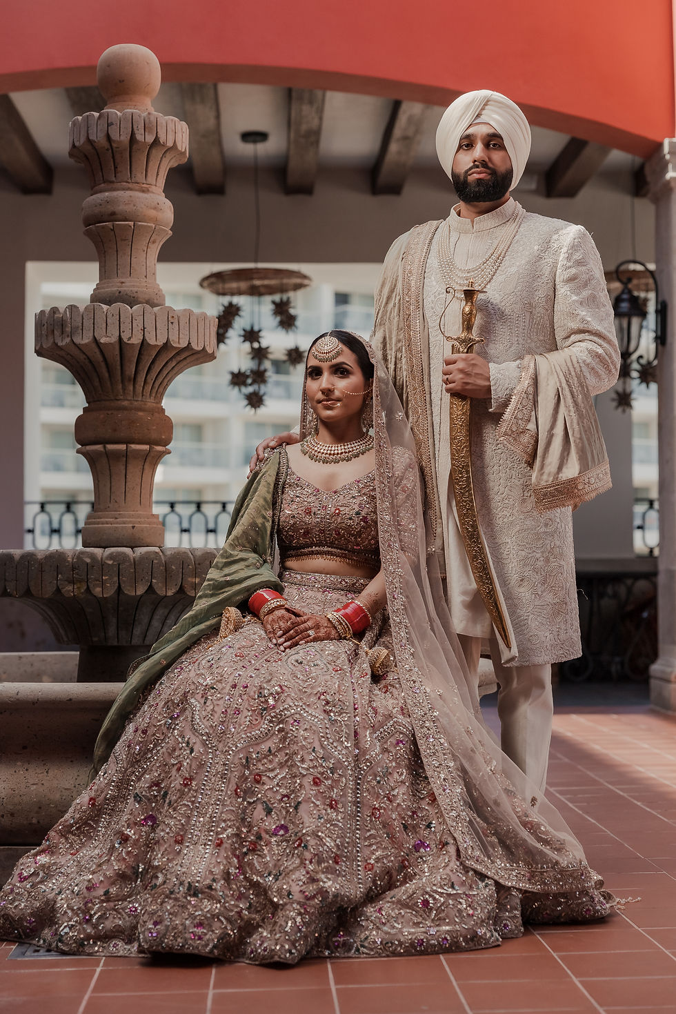Sikh groom with sword and Indian bride in heavily embroidered lehenga pose regally at Royalton Riviera Cancun during their destination wedding in Mexico.