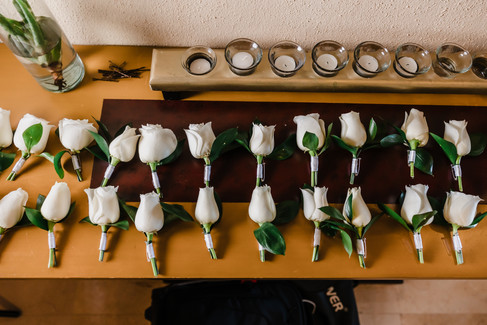 Rows of white rose boutonnieres neatly arranged on a wooden table at Garza Blanca Puerto Vallarta, ready for groomsmen and family members before the wedding ceremony.
