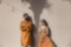 Stylish Indian bride and groom in traditional wedding attire posing against a sunlit wall with palm tree shadows during their destination wedding in Mexico.