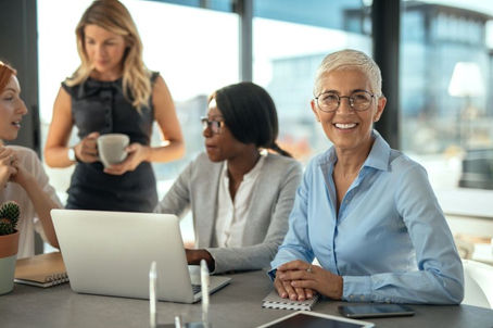 Photo or an older female professional in an office with young people conveying how aging workers can maintain relevance.