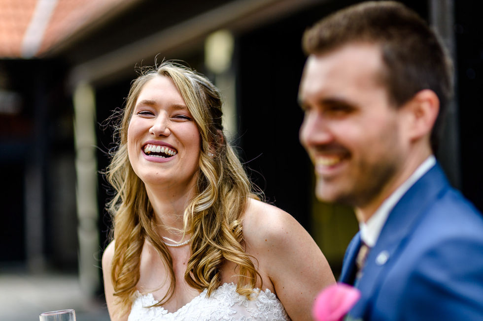 Braut steht neben Braeutigam und lacht strahlend in die Kamera.