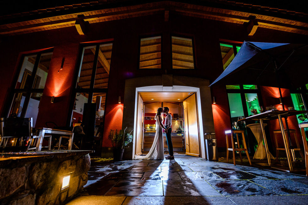 Brautpaar steht sich bei Nacht vor beleuchteter Hausfassade gegenueber-das Hochzeitsbild wurde von Hochzeitsfotograf Roger Rachel Photography in der Hochzeitslocation Pauls Vinothek in der Pfalz fotografiert