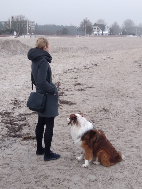 Coach Anika und Hund am Meer in Richtung Land guckend.