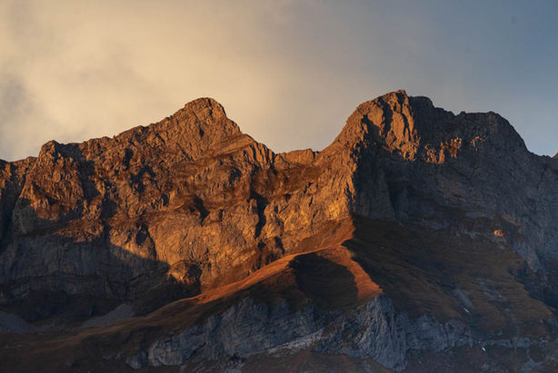 Sunset with a view from Titlis mountain to the other side of the valley. The sun lights up the top of the peaks in a soft orange.