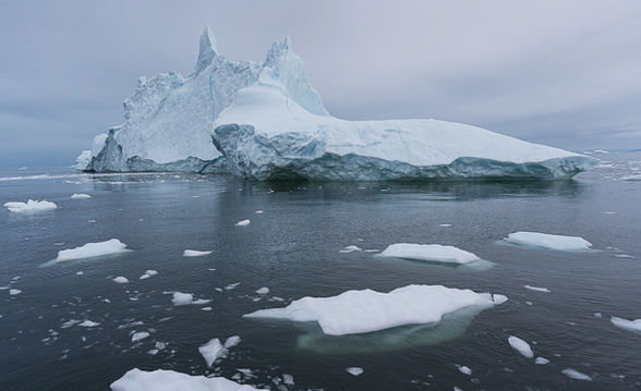 An iceberg in calm water with icefloes in front.