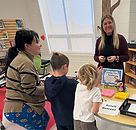 Adults engaging with two students looking at books.