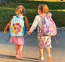 Two students holding hands walking to school wih backpacks on.