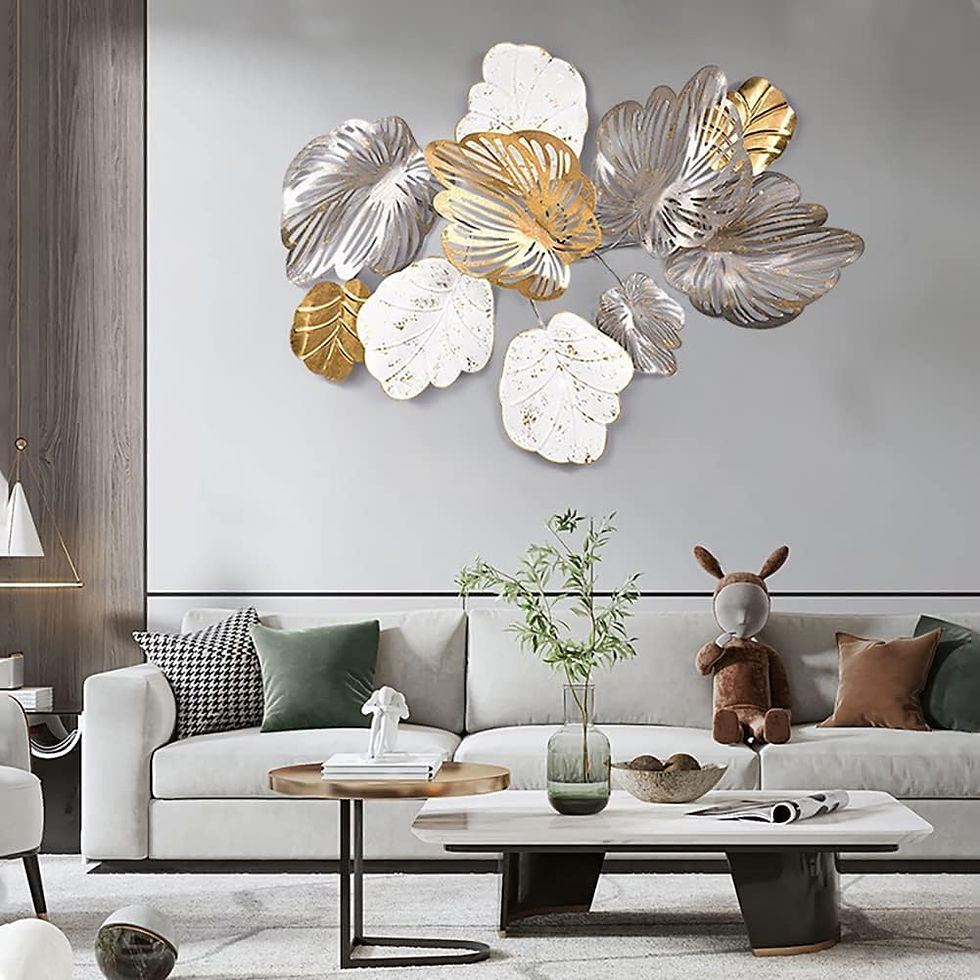 Modern living room with a gray sofa, plush toy, and decorative pillows. Gold and silver leaf wall art above a coffee table with plants. Neutral tones.