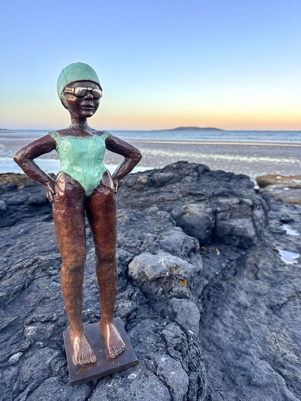 Thumbnail: “Bronze swimmer sculpture in vintage swimsuit and cap standing confidently on coastal rocks at sunset; Dawn Conn figurative