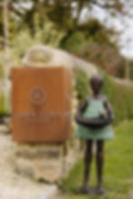 Thumbnail: Bronze girl in a green dress holding a birdbath bowl beside the Dawn Conn Sculpture sign in a garden setting.