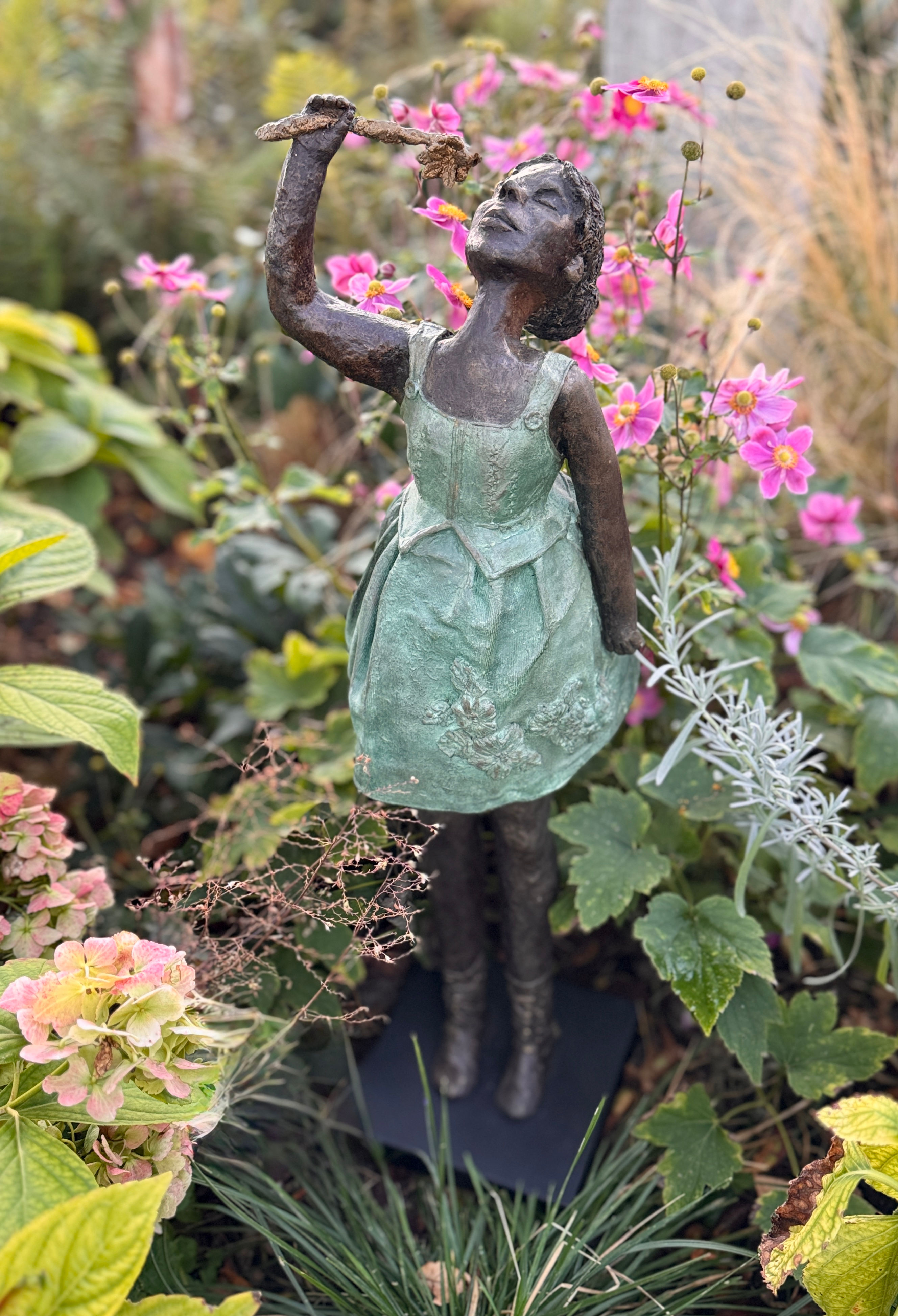 Bronze figurative sculpture of a girl holding a flower in a garden