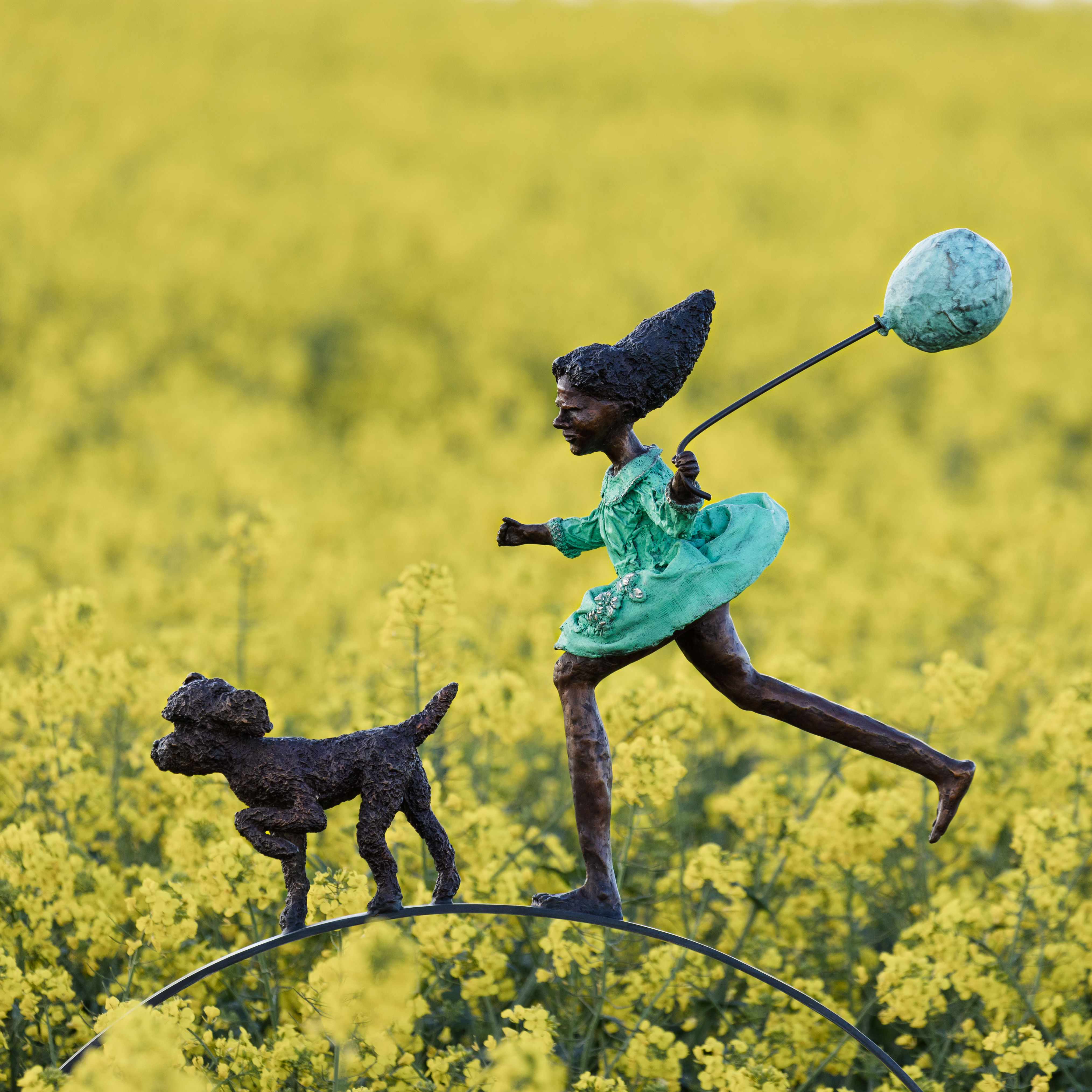 bronze sculpture of girl running behind a dog with a Verdigris green dress holding a balloon