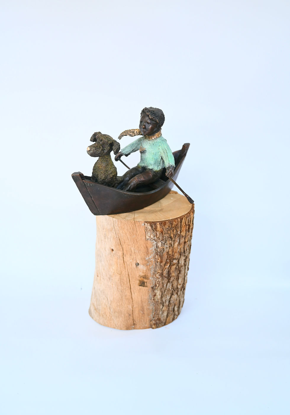 Thumbnail: Bronze boy and dog seated in narrow boat, showing jumper’s ribbed texture, oars, and warm patina across figures and vessel.